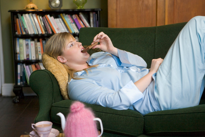 A young woman lying on her couch eating chocolate