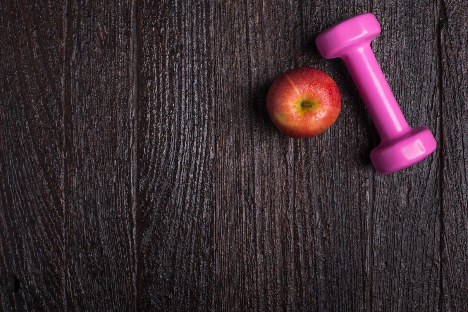 Dumbbell and apple on dark wooden background to illustrate Feminine Odor After Gastric Sleeve
