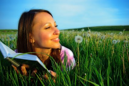 A woman reading a book in a lush green field