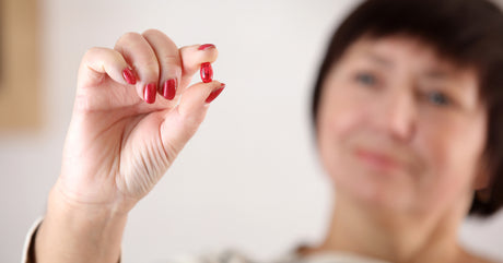 A smiling woman slightly burred holding a red pill in focus to help illustrate bariatric probiotics