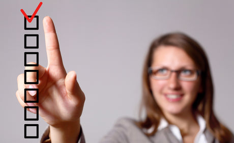 A blurred woman in the background makes a red check with her finger on a clear checklist in the foreground to illustrate checklist for bariatric surgery.