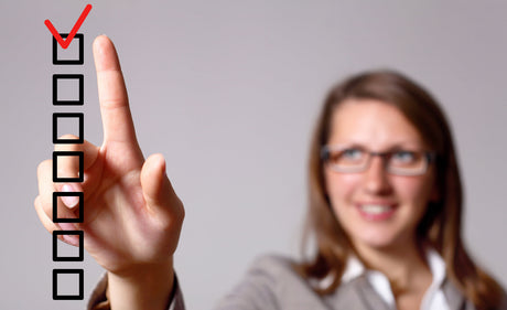 A blurred woman in the background makes a red check with her finger on a clear checklist in the foreground to illustrate checklist for bariatric surgery.