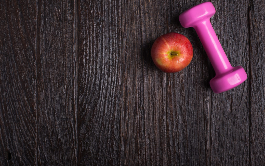 Dumbbell and apple on dark wooden background to illustrate Feminine Odor After Gastric Sleeve