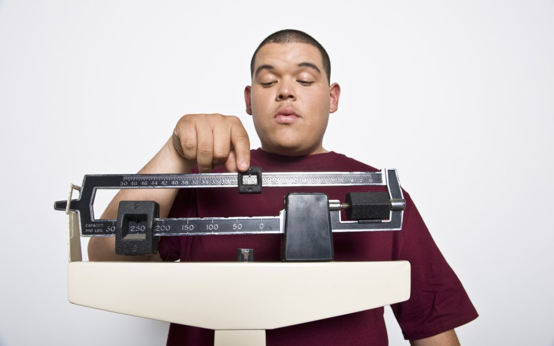 young man weighs himself on a scale to illustrate How Overweight To Get Bariatric Surgery