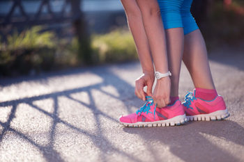 Closeup of jogging woman tying running shoe to help illustrate reasons for weight gain in females.