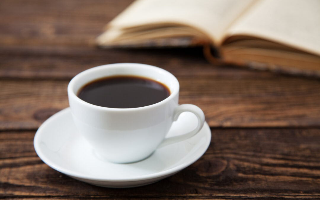 A mug of coffee next to a book on a wood table to help illustrate caffeine after gastric sleeve