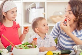 A mother and her two young children are seen eating fresh vegetables.