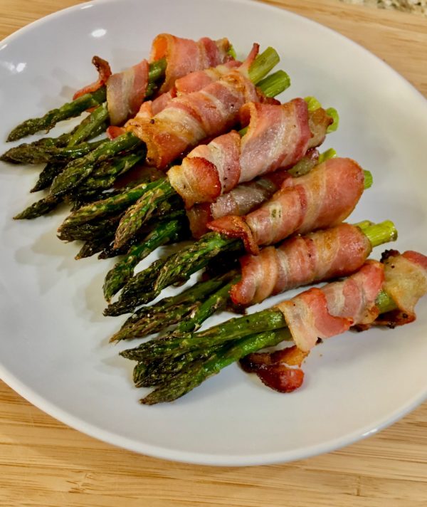 An image of bacon wrapped asparagus on a white plate