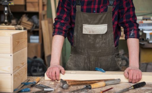 A woodworker in his shop holding a piece of wood to help illustrate Gastric Bypass Recovery Time Off Work. 